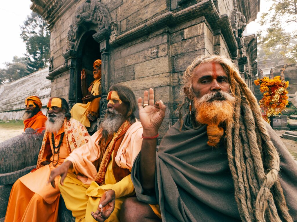 Hindu sadhus with traditional attire and dreadlocks sitting outside a temple.