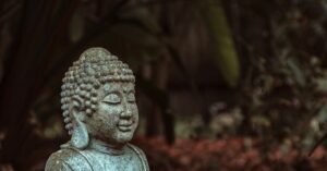 A peaceful stone Buddha statue amidst green foliage in an outdoor garden, evoking tranquility.
