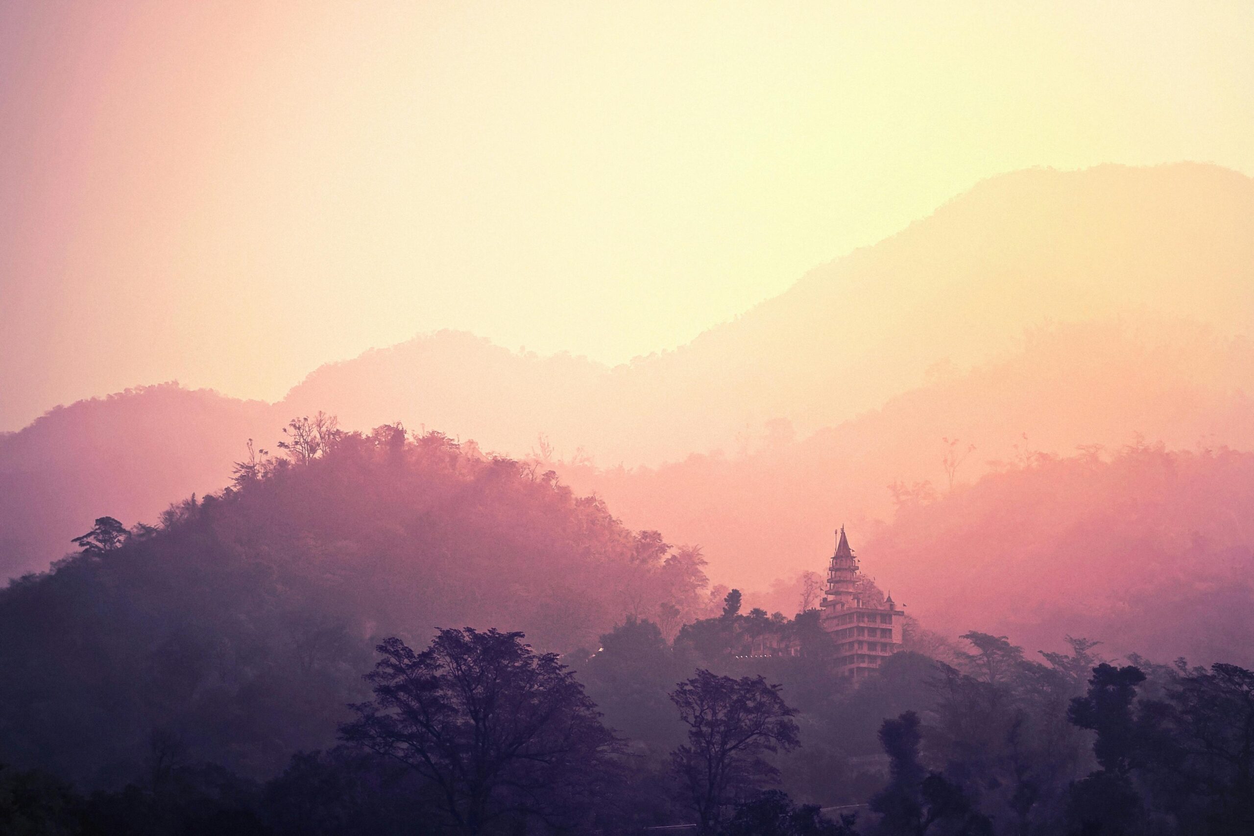 A tranquil view of Rishikesh mountains and temple enveloped in pink hues at sunrise.